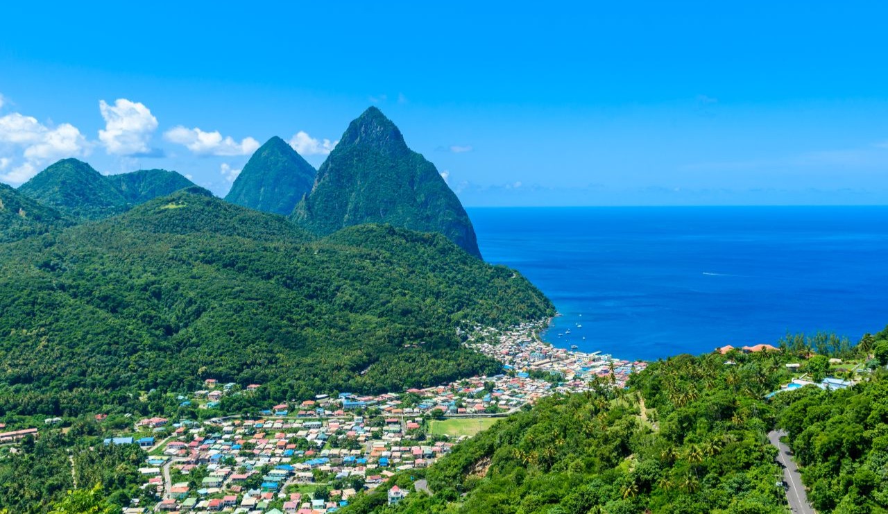 A photo of The Pitons, two mountains in Saint Lucia, with a clear sky and bright blue sea to the right.