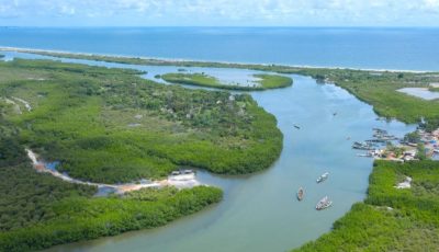Aerial photo of the river Gambie's entry to the Atlantic Ocean, with the sea and horizon in the background, lush green around the river in the foreground.