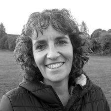 Profile photo of Kerry Meek, Education Officer. Kerry wears a dark top and gilet, and is smiling at the camera. Photo is in greyscale.