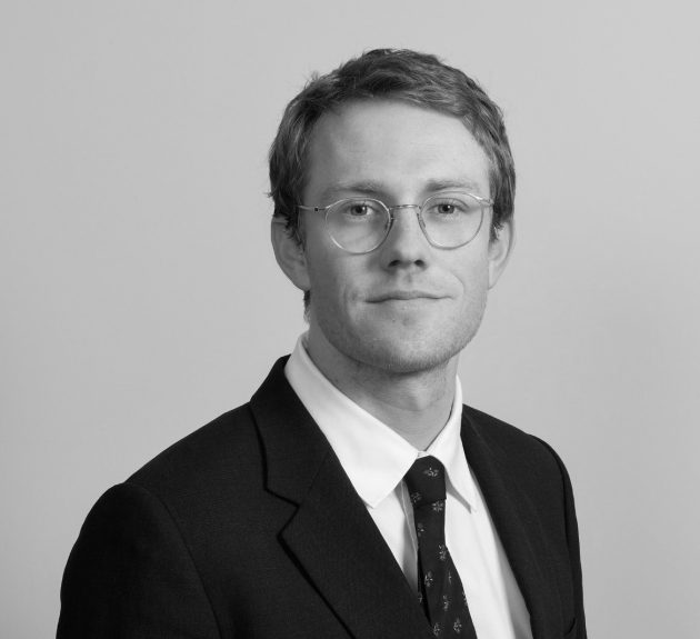 Profile photo of Patrick Cumming, Data Modelling Lead at Common Seas. Patrick wears a dark blazer, white shirt and dark tie, with glasses. He is looking at the camera slightly smiling. Photo is in greyscale.