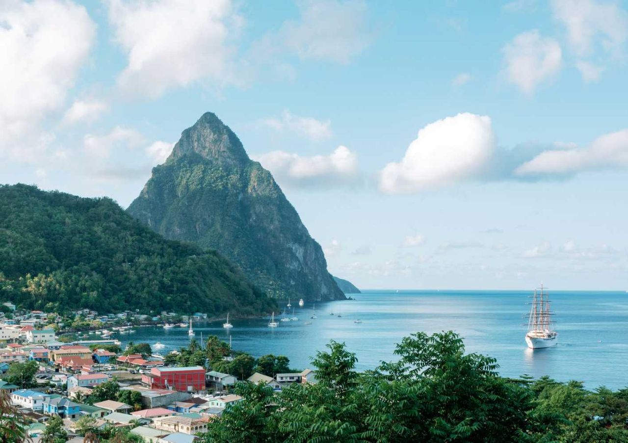 Photo along the coast of Saint Lucia towards the mountains, known as The Pitons. The sky and sea are blue, with dark green rainforest in the foreground.