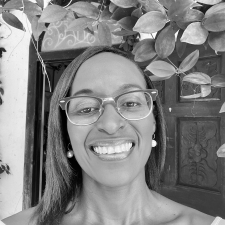 Profile photo of Stacey Alvarez de la Campa. Stacey wears a striped collared shift and glasses. She smiles at the camera. Photo is in greyscale