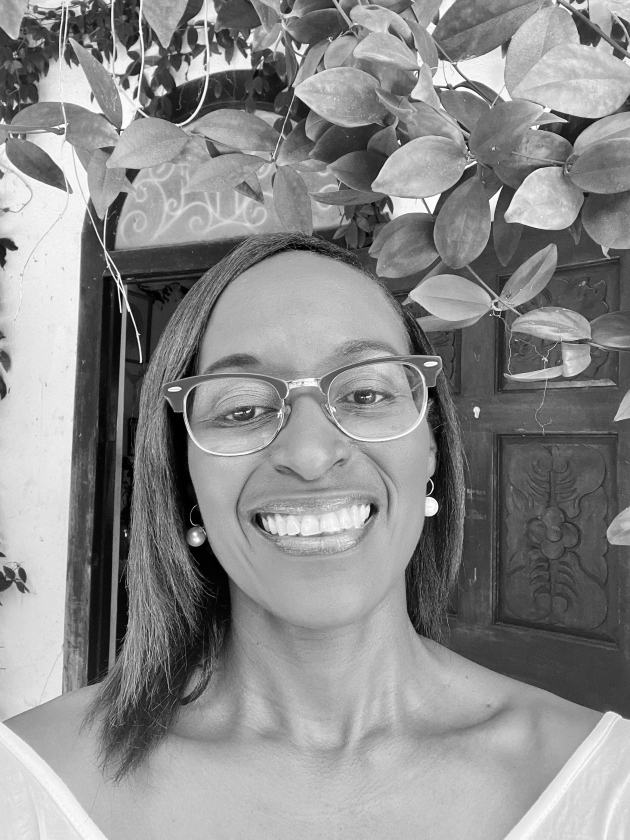 Profile photo of Stacey Alvarez de la Campa. Stacey wears a striped collared shift and glasses. She smiles at the camera. Photo is in greyscale