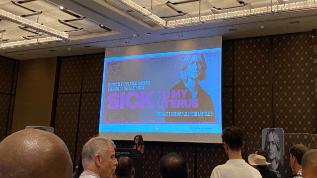 Indoor event at INC5.2 in Geneva for the Minderoo PlasticHealthAware dashboard launch. An image is on a screen of a woman with a caption reading 'sick to my uterus'