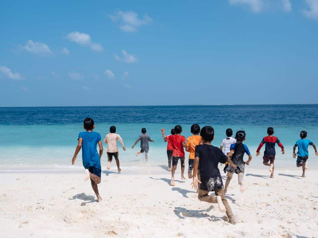 Children running across white sand into the seas in Maldives