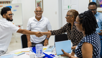 Saint Lucia workshop - Five Saint Lucians at the workshop celebrating its success. A man and a woman are shaking hands and smiling. Another three people are in the group. All stand in a room with while walls.