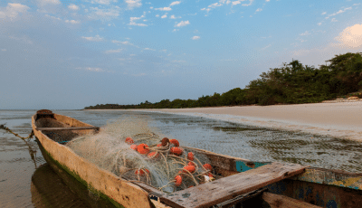 Financial assessment of policies to tackle plastic pollution in Guinea-Bissau. Small wooden wishing boat on edge of beach with net and buoys inside.