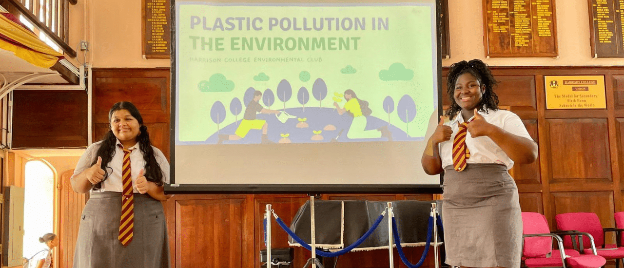 Barbados leads sustainability education with Harrison College becoming the first Plastic Clever School in the Caribbean Photo: students presenting on plastic pollution i the environment at Harrison College - two female presenting students stand in from of projector screen giving thumbs up